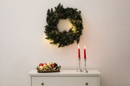Christmas decor and burning candles on cabinet near white wall indoorsの写真素材