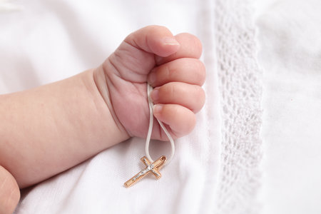 Sacrament of baptism. Little baby holding gold cross on bed, closeupの写真素材