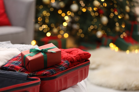 Christmas vacation. Suitcase with clothes and gift box on floor indoors, closeup. Space for textの写真素材