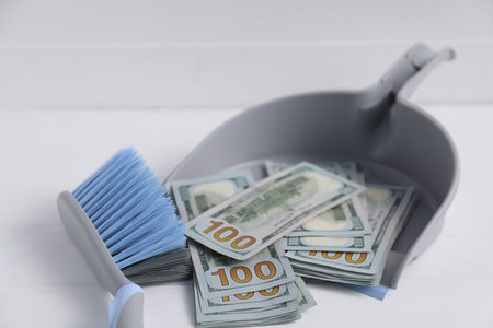 Dustpan with broom and dollar banknotes on white background, closeup. Space for textの写真素材