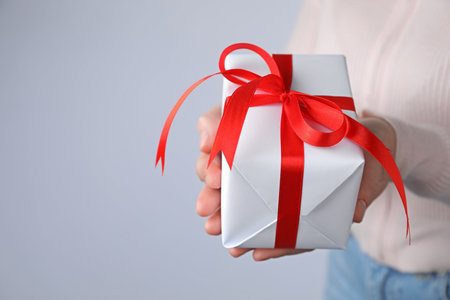 Woman with gift box on gray background, closeup. Space for textの写真素材