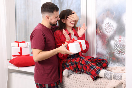 Happy boyfriend surprising his girlfriend with Christmas gift at homeの写真素材