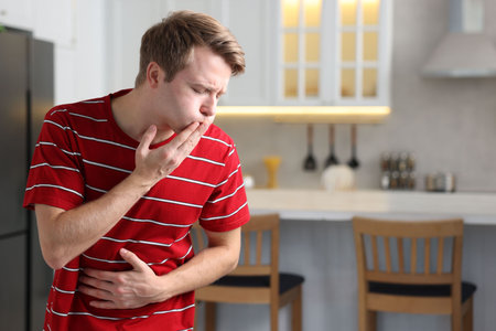 Young man suffering from nausea and stomachache indoors, space for text
