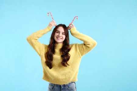 Portrait of smiling woman in sweater having fun with candy canes on light blue background.の写真素材
