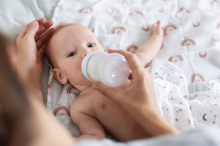 Mother feeding her little baby with bottle on bed, closeupの写真素材