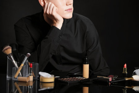 Makeup artist with tools and cosmetic products at table on black background. Space for textの写真素材