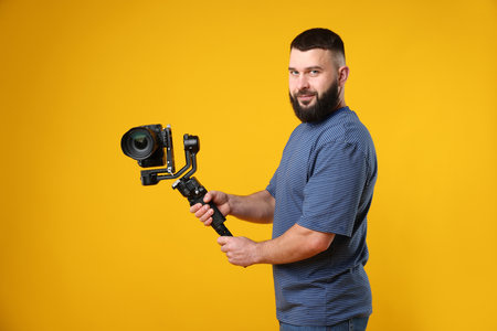 Videographer using gimbal stabilizer with camera on yellow backgroundの写真素材