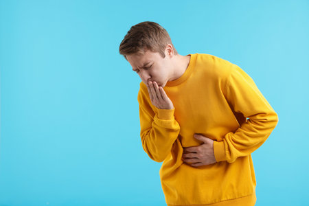 Young man suffering from nausea and stomachache on light blue background, space for textの写真素材