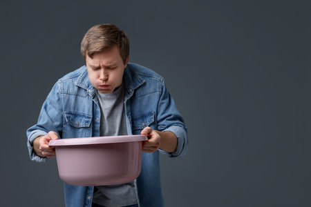 Young man with basin suffering from nausea on gray background, space for textの写真素材