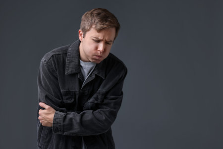 Young man suffering from nausea and stomachache on gray background, space for textの写真素材