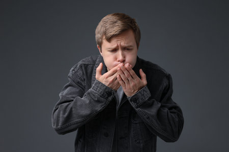 Young man suffering from nausea on gray backgroundの写真素材