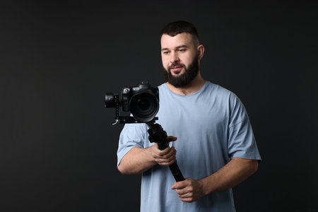 Videographer using gimbal stabilizer with camera on black background. Space for textの写真素材