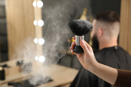 Hairstylist holding brush with talcum powder and her client at salon, selective focus. Space for textの写真素材