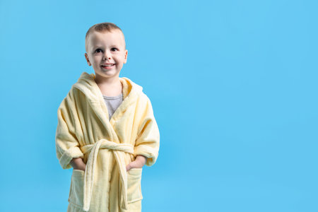 Smiling little boy in yellow bathrobe on light blue background. Space for textの写真素材