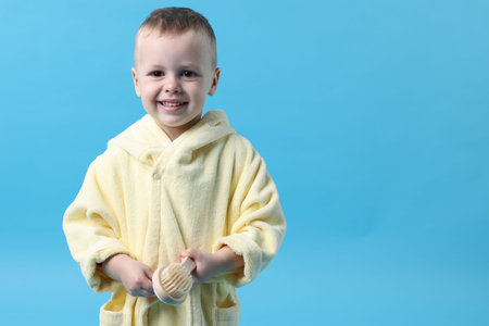 Smiling little boy in yellow bathrobe on light blue background. Space for textの写真素材
