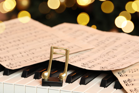 Golden music notes and sheets on piano near Christmas tree, closeup. Bokeh effectの写真素材
