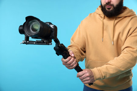 Videographer using gimbal stabilizer with camera on light blue background, closeup