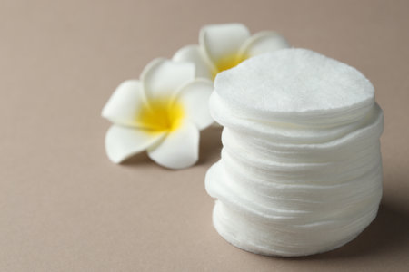 Stack of clean cotton pads and plumeria flowers on beige background, closeup. Space for textの写真素材