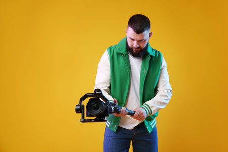 Videographer using gimbal stabilizer with camera on yellow background. Space for textの写真素材