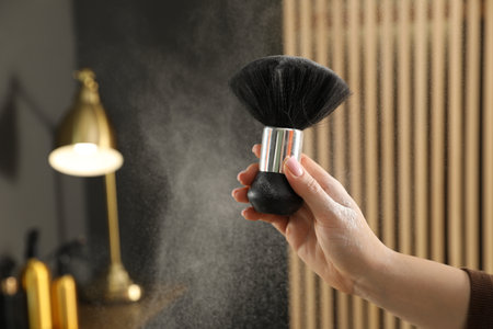Hairstylist holding brush with talcum powder at salon, closeup. Space for text
