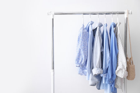 Different stylish clothes and bag hanging on rack near white wall indoors, space for textの写真素材
