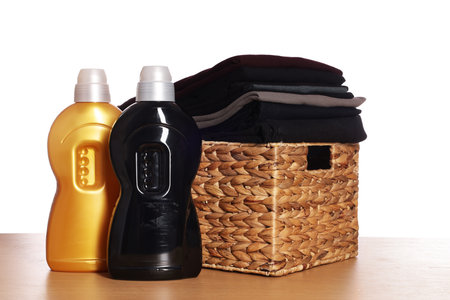 Laundry basket with clean clothes and detergents on wooden table against white backgroundの写真素材