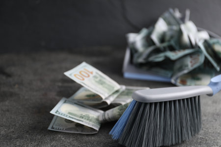Dustpan with broom and dollar banknotes on gray background, selective focus. Space for textの写真素材