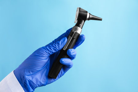 Doctor with otoscope on light blue background, closeupの写真素材