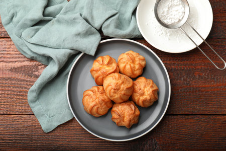 Fresh tasty profiteroles and powdered sugar on wooden table, top viewの写真素材