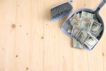 Dustpan with broom and dollar banknotes on wooden background, flat lay. Space for textの写真素材