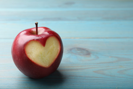 Red apple with carved heart on blue wooden table, closeup. Space for textの写真素材