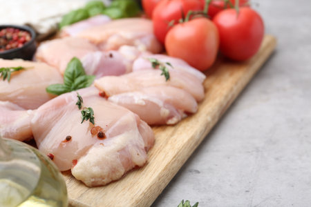 Raw chicken thighs with herbs, peppercorns and tomatoes on light table, closeupの写真素材
