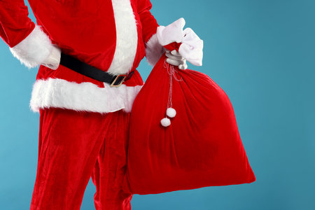 Santa Claus holding sack on light blue background, closeup. Merry Christmas and Happy New Yearの写真素材