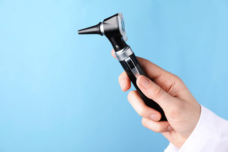 Doctor with otoscope on light blue background, closeup. Space for textの写真素材