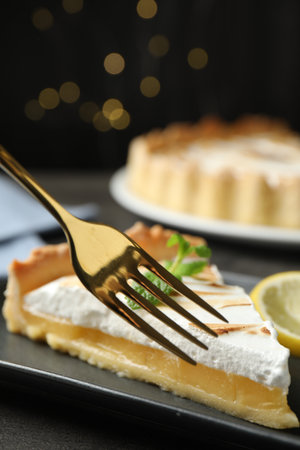 Eating slice of tasty lemon meringue tart with fork on black table, closeupの写真素材