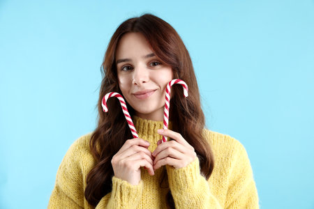 Portrait of beautiful woman in sweater with candy canes on light blue background.の写真素材