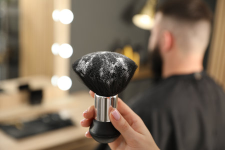 Hairstylist holding brush with talcum powder and her client at salon, selective focusの写真素材