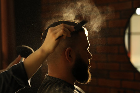 Hairstylist applying talcum powder with brush and comb onto man's hair at salon, closeupの写真素材