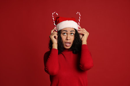 Beautiful woman with Santa hat and candy canes on red background. Christmas seasonの写真素材