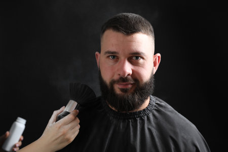 Hairstylist applying talcum powder with brush on her client against black background, closeupの写真素材
