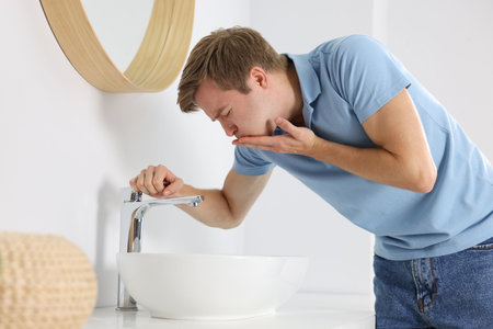 Young man suffering from nausea over sink in bathroomの写真素材