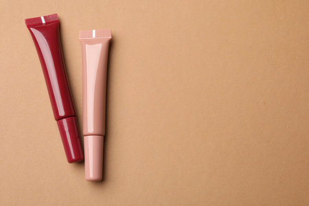 Different lip glosses on brown background, flat lay. Space for textの写真素材