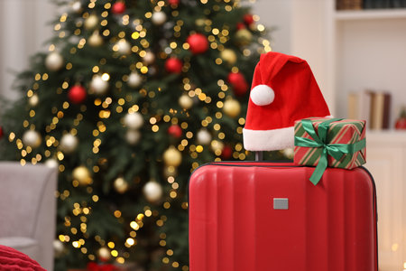 Christmas vacation. Suitcase with Santa hat and gift box indoors, closeup. Space for textの写真素材