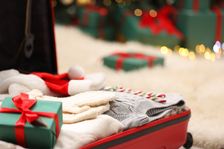 Christmas vacation. Suitcase with Santa hat, clothes and gift box on floor indoors, closeupの写真素材