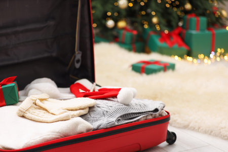 Christmas vacation. Suitcase with Santa hat, clothes and gift box on floor indoors, closeup. Space for textの写真素材