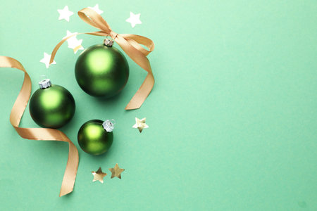 Beautiful Christmas composition with baubles, golden ribbon and confetti on green background, flat lay. Space for textの写真素材