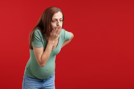 Pregnant woman suffering from nausea on red background. Space for textの写真素材
