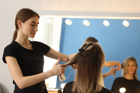 Hairdresser cutting woman's hair near mirror in beauty salonの写真素材