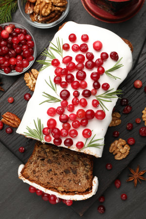 Tasty Christmas cake with icing, cranberries, nuts, spices and festive decor on black table, flat layの写真素材