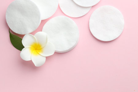 Clean cotton pads and plumeria flower on pink background, flat lay. Space for textの写真素材